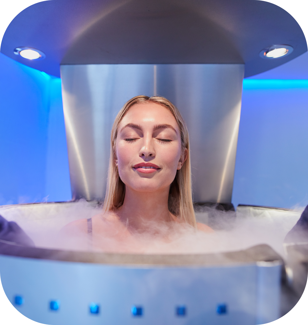 Woman receiving whole-body cryotherapy in a silver chamber surrounded by cold vapor, illustrating a wellness treatment available through Cherry financing